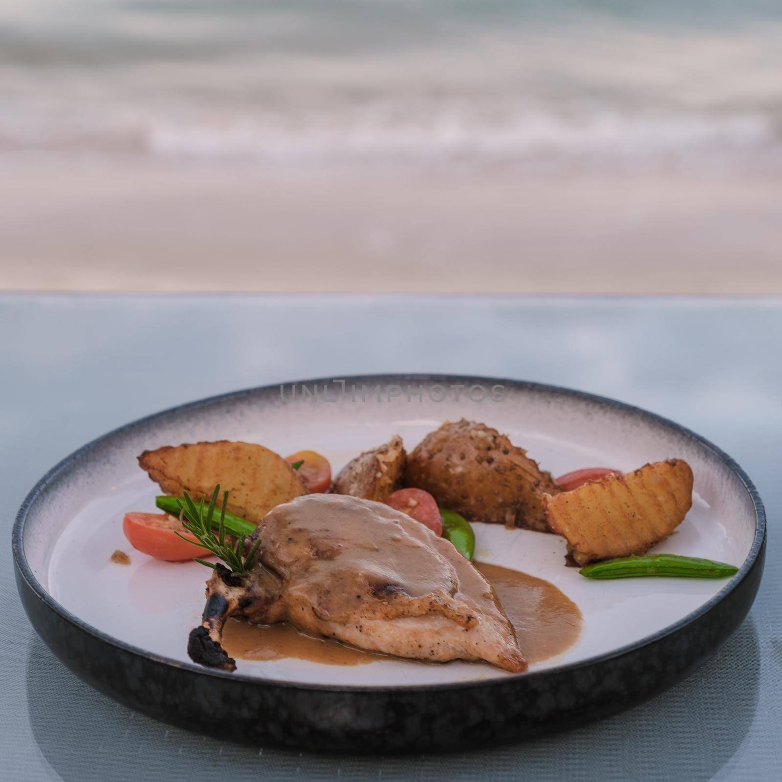 grilled lamb veal ribs loin on a plate with baked potatoes, dinner on beach