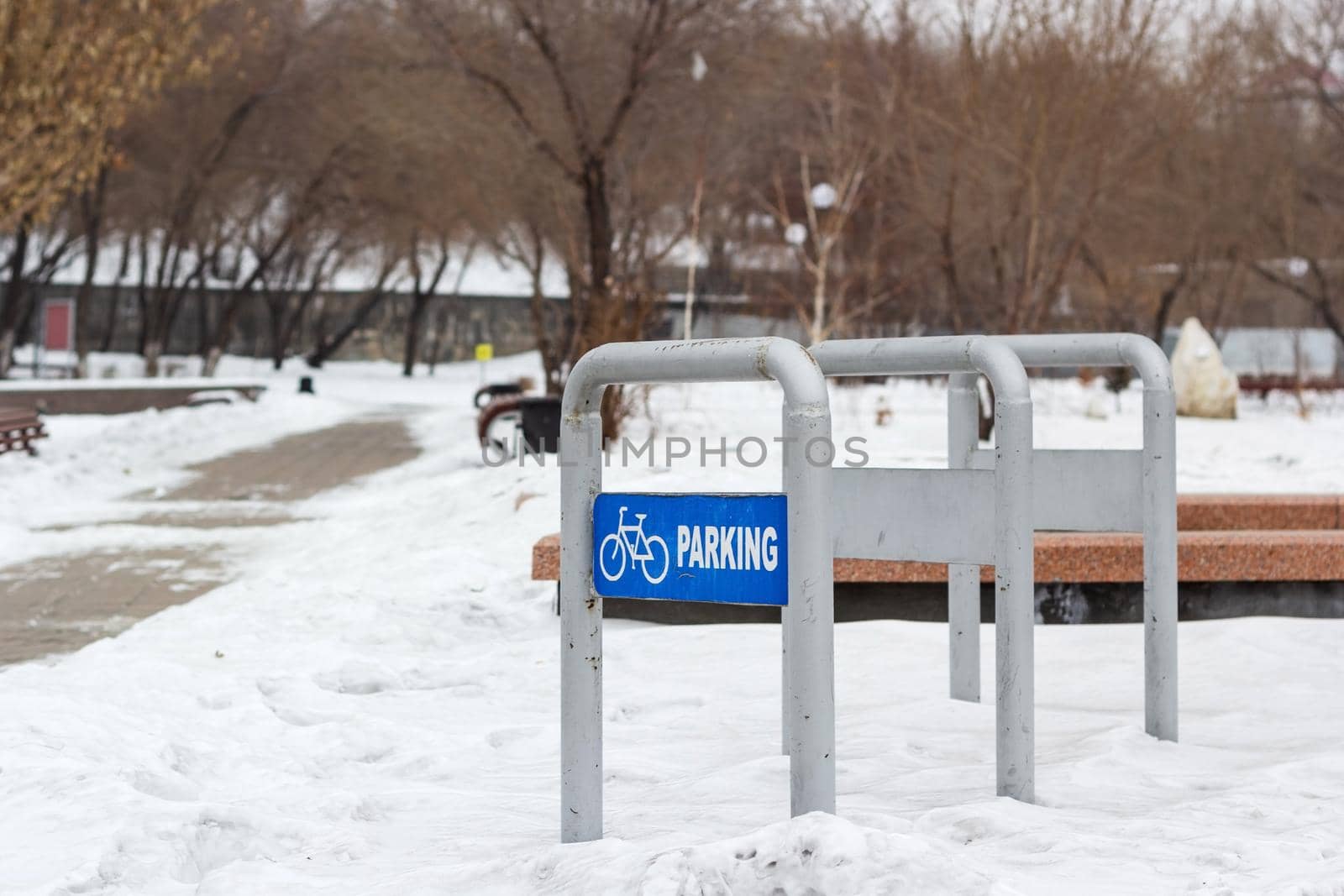 Empty bike parking in snowy public park at cold white winter, urban bicycle station in city recreation zone with cloudy weather