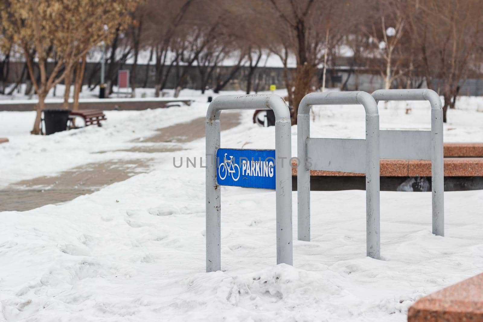Empty bike parking in snowy public park at cold white winter, urban bicycle station in city recreation zone with cloudy weather