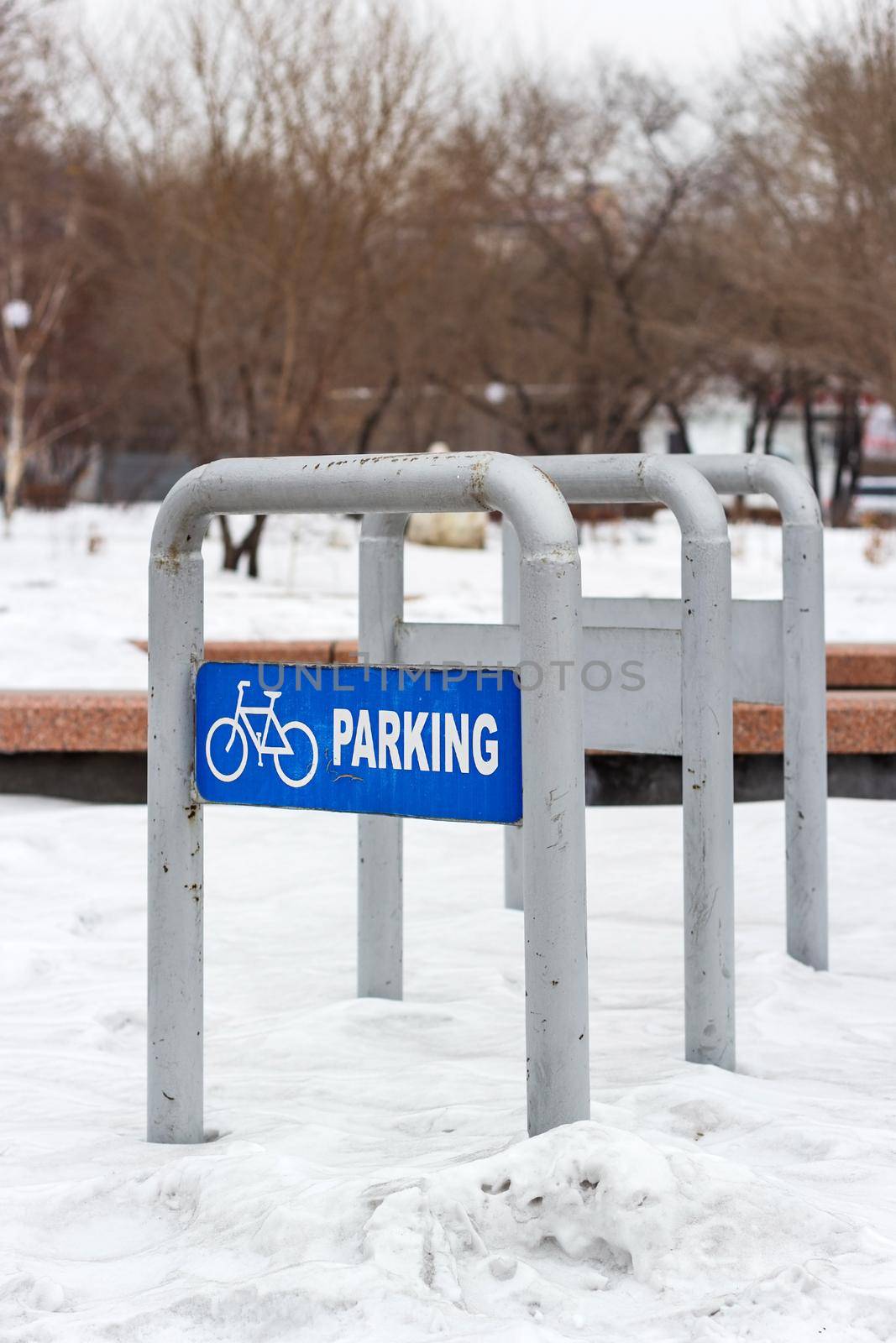 Empty bike parking in snowy public park at cold white winter, urban bicycle station in city recreation zone with cloudy weather, vertical image