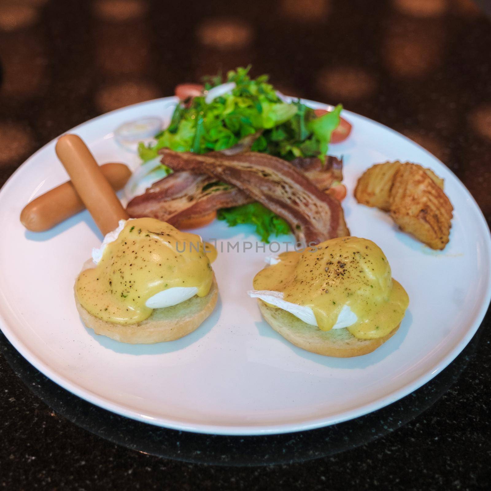 Egg benedict isolated on a plate with salad and sausage and cream hollandaise sauce