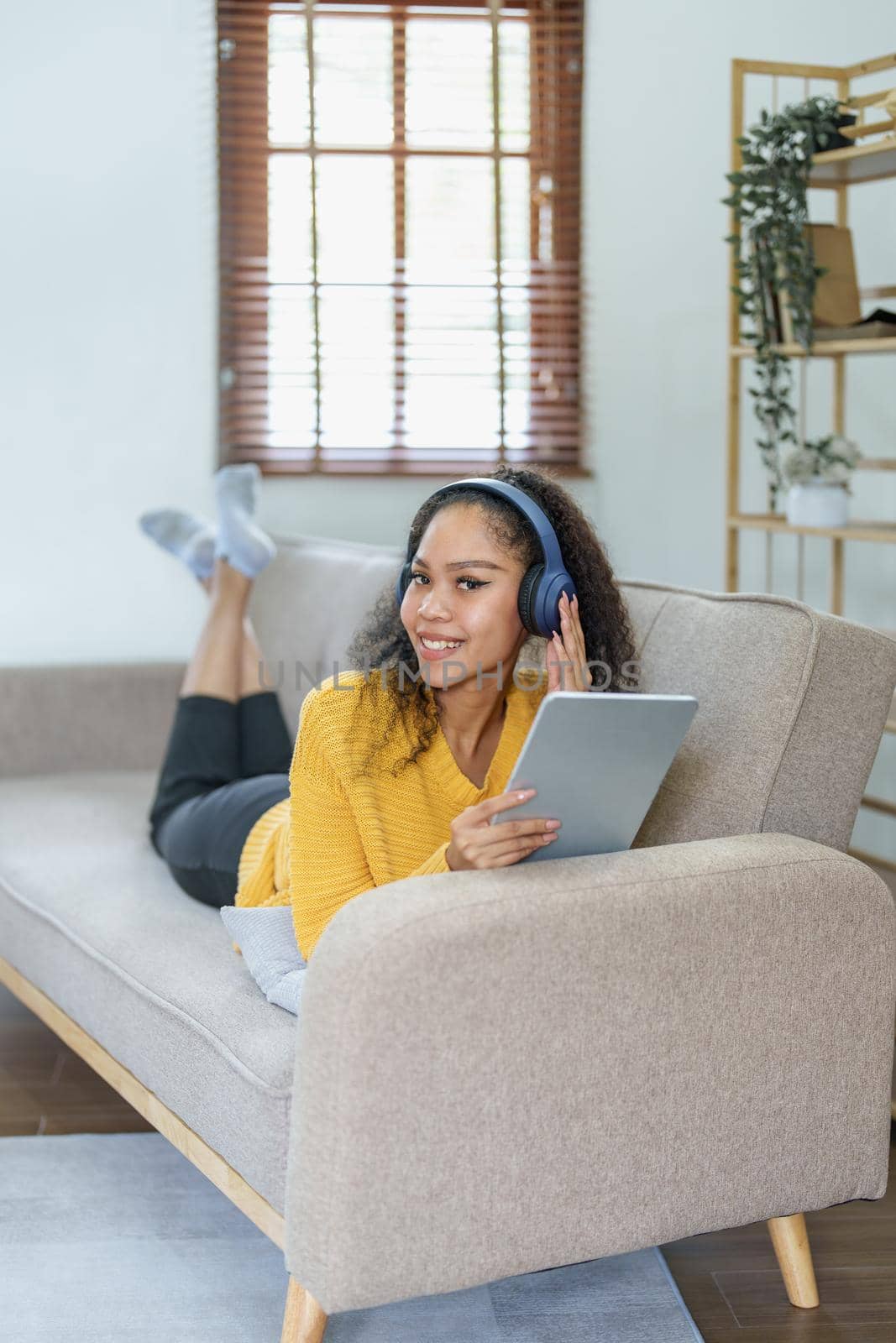 Portrait of an African American sitting on a sofa using tablet and wearing headphones to relax.