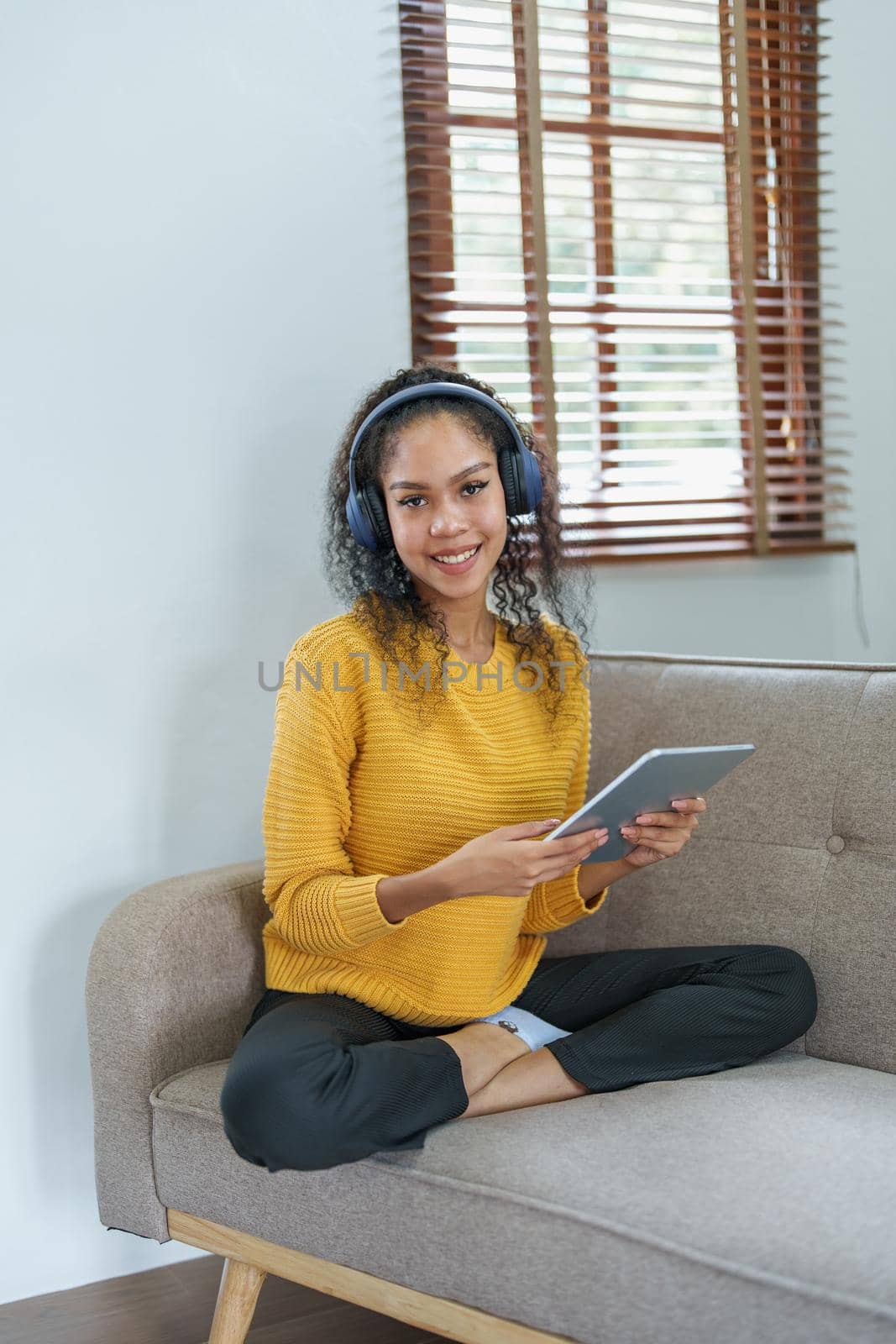 frican American sitting on a sofa using tablet and wearing headphones to relax by Manastrong