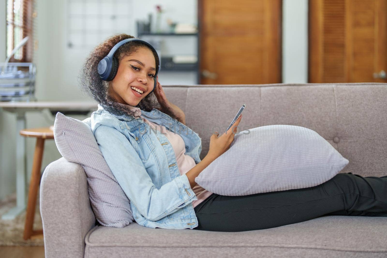 Portrait of an African American sitting on a sofa using a phone and wearing headphones to relax.