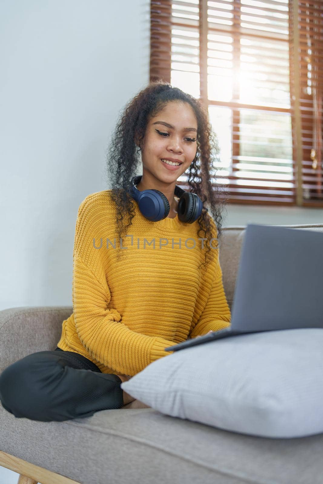 Portrait of an African American sitting on the sofa wearing on-ear headphones and using a computer at home.