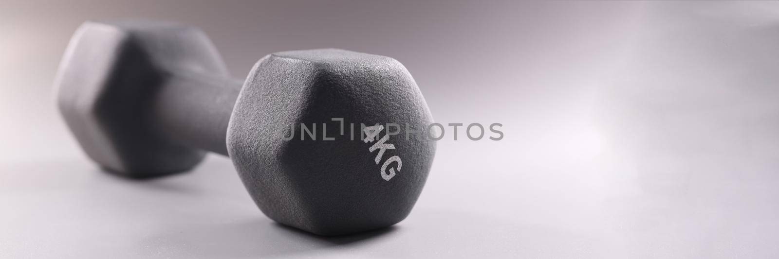 Black sports dumbbell for bodybuilding on gray background closeup. Sale of sports accessories concept