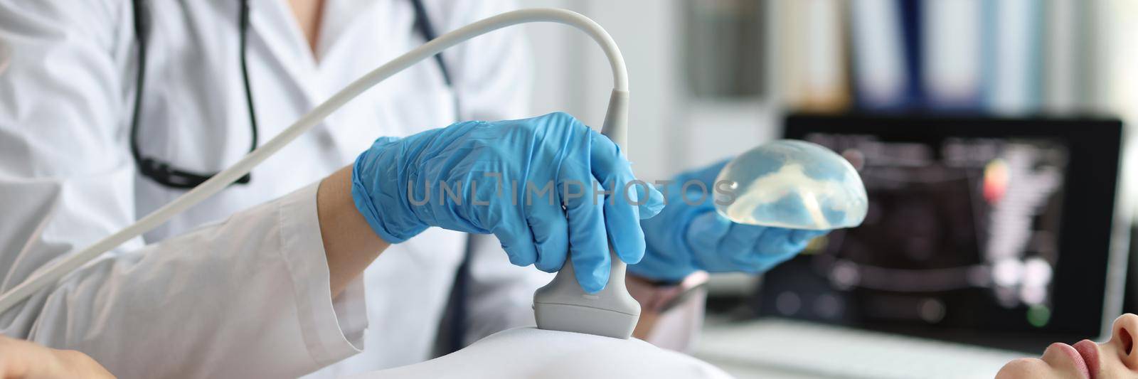 Doctor holding implant and doing ultrasound examination of woman breasts closeup. Annual preventive ultrasound examinations after mammoplasty concept