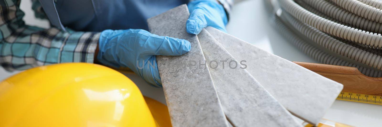 Builder holding gray tiles for bathroom in workshop closeup. Apartment decoration concept