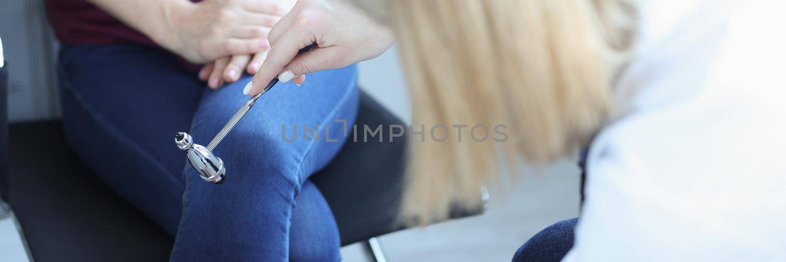 Doctor neurologist checking knee reflexes to female patient with percussion hammer in clinic closeup by kuprevich