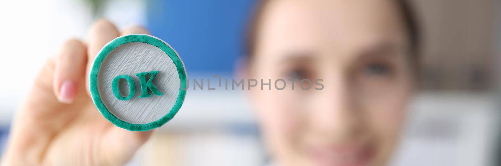 Woman holding green ink stamp OK in her hand closeup.