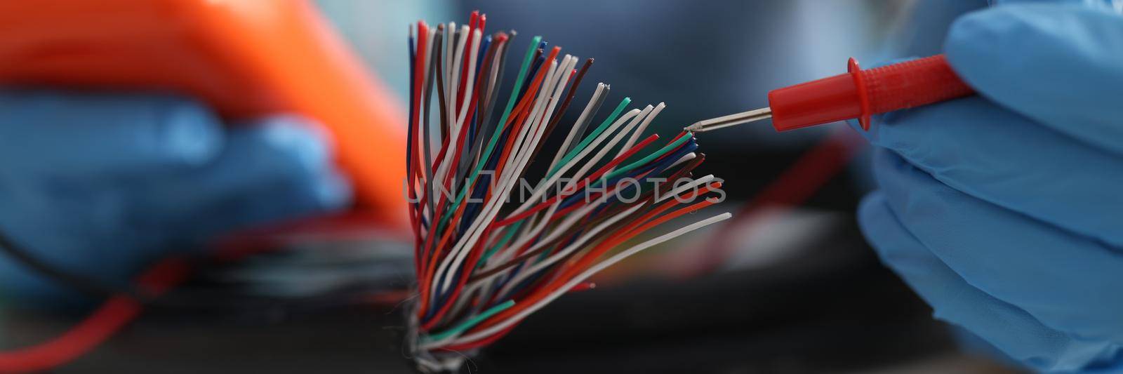 Master repairman testing multicolored wires from cable using tester closeup. Electronics repair concept