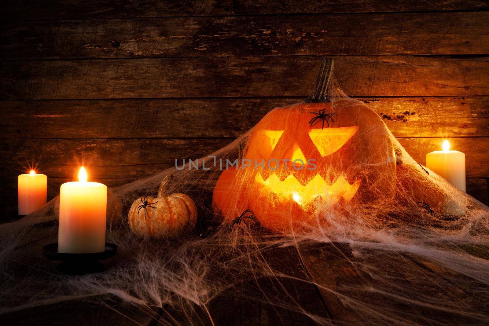 Festive mystical halloween interior. Pumpkin, spider web, burning candles, spiders on dark wooden background