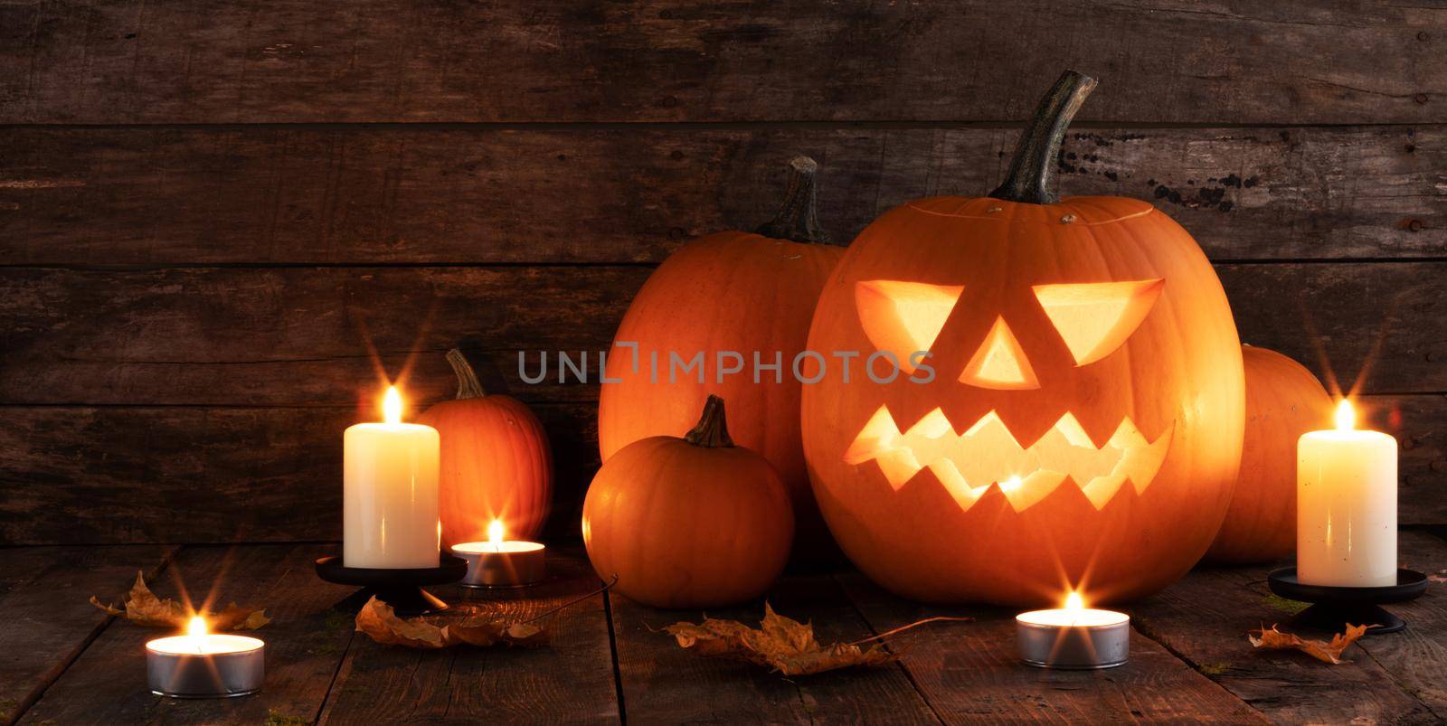 Halloween pumpkins candles and dry maple leaves on wooden background