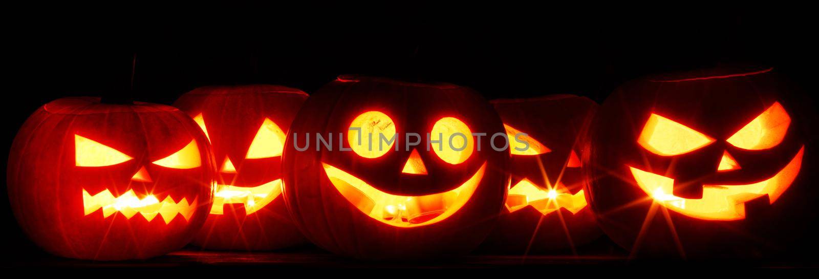 Five Halloween glowing lantern pumpkins in a row on dark background