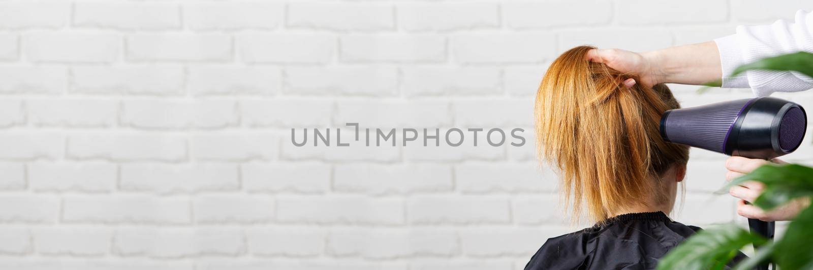 Beautiful young woman at the hairdresser blow drying her hair. Hair dryer in salon by PhotoTime