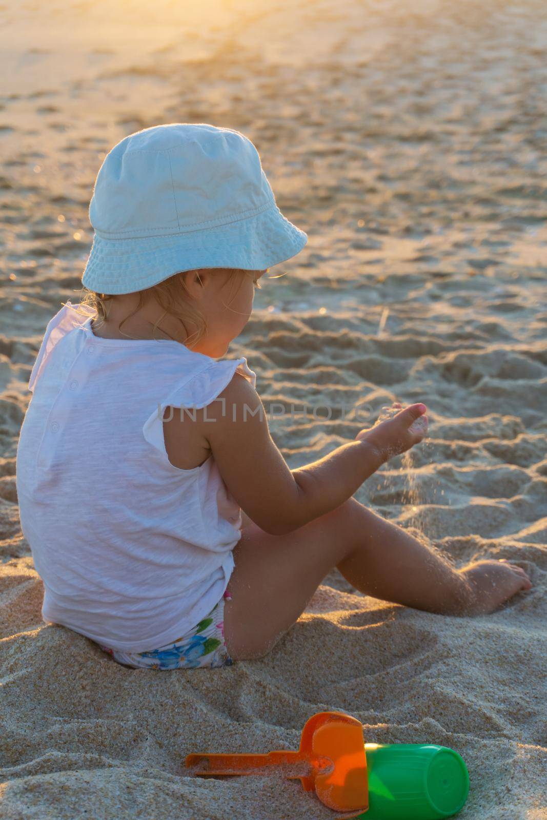 Little girl in a panama hat plays with sand on the beach