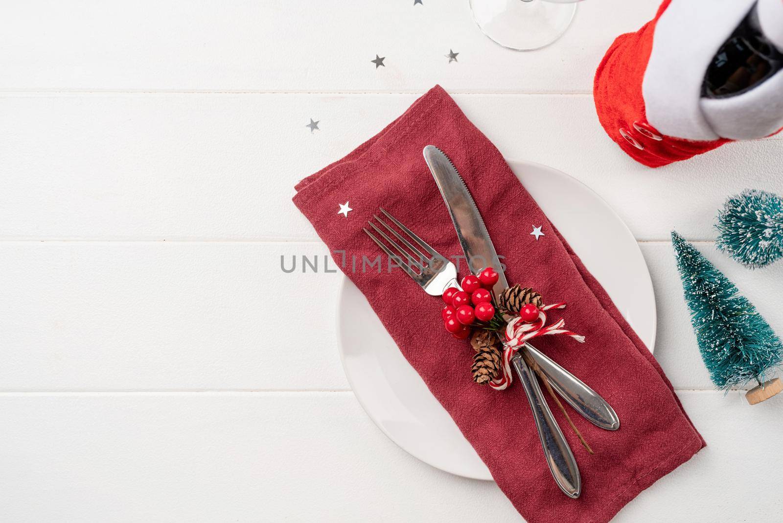 Christmas table setting with white dishware, silverware and red and green decorations on white wooden background. Top view, flat lay copy space
