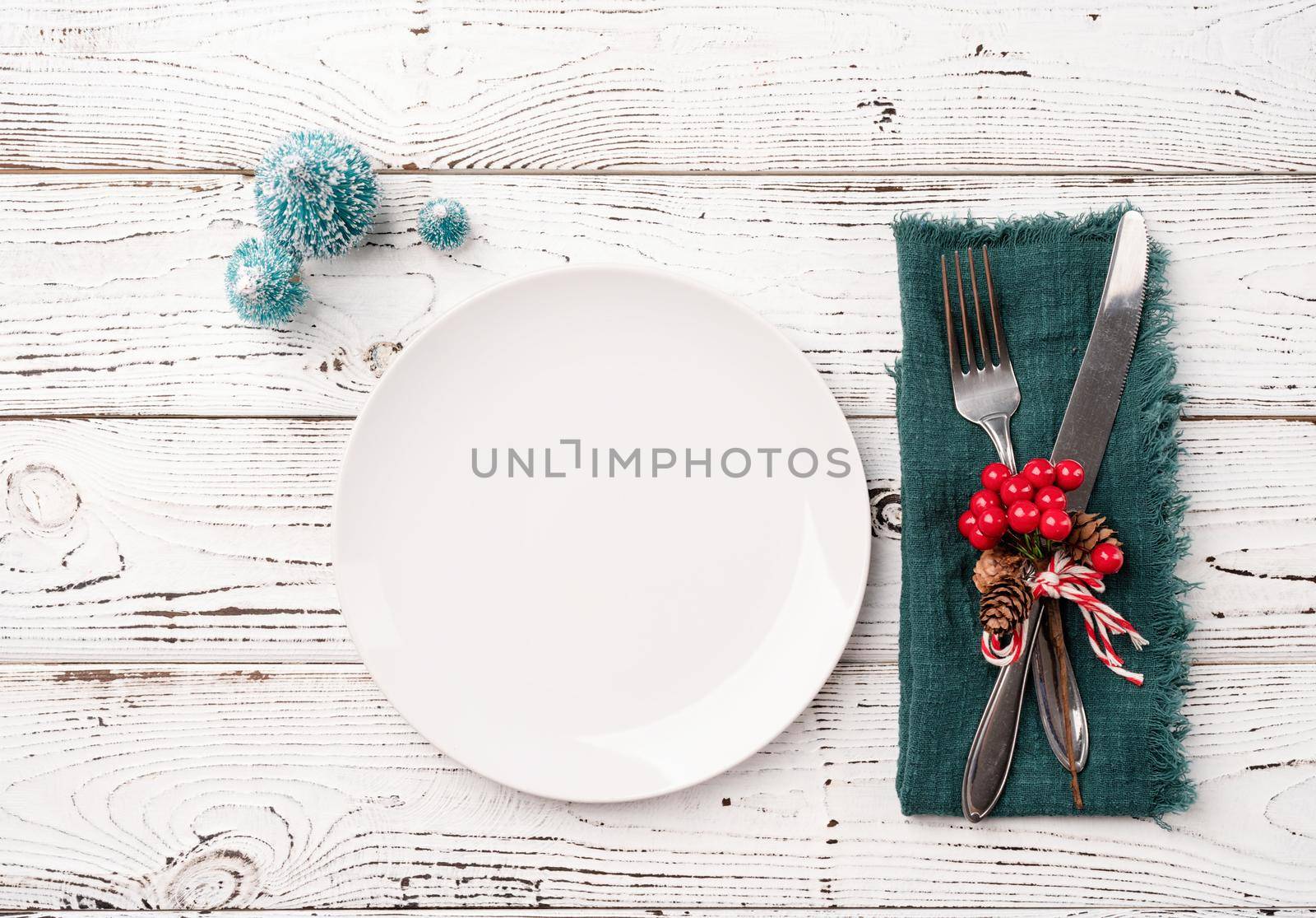 Christmas table setting with white dishware, silverware and red and green decorations on white wooden background. Top view, flat lay