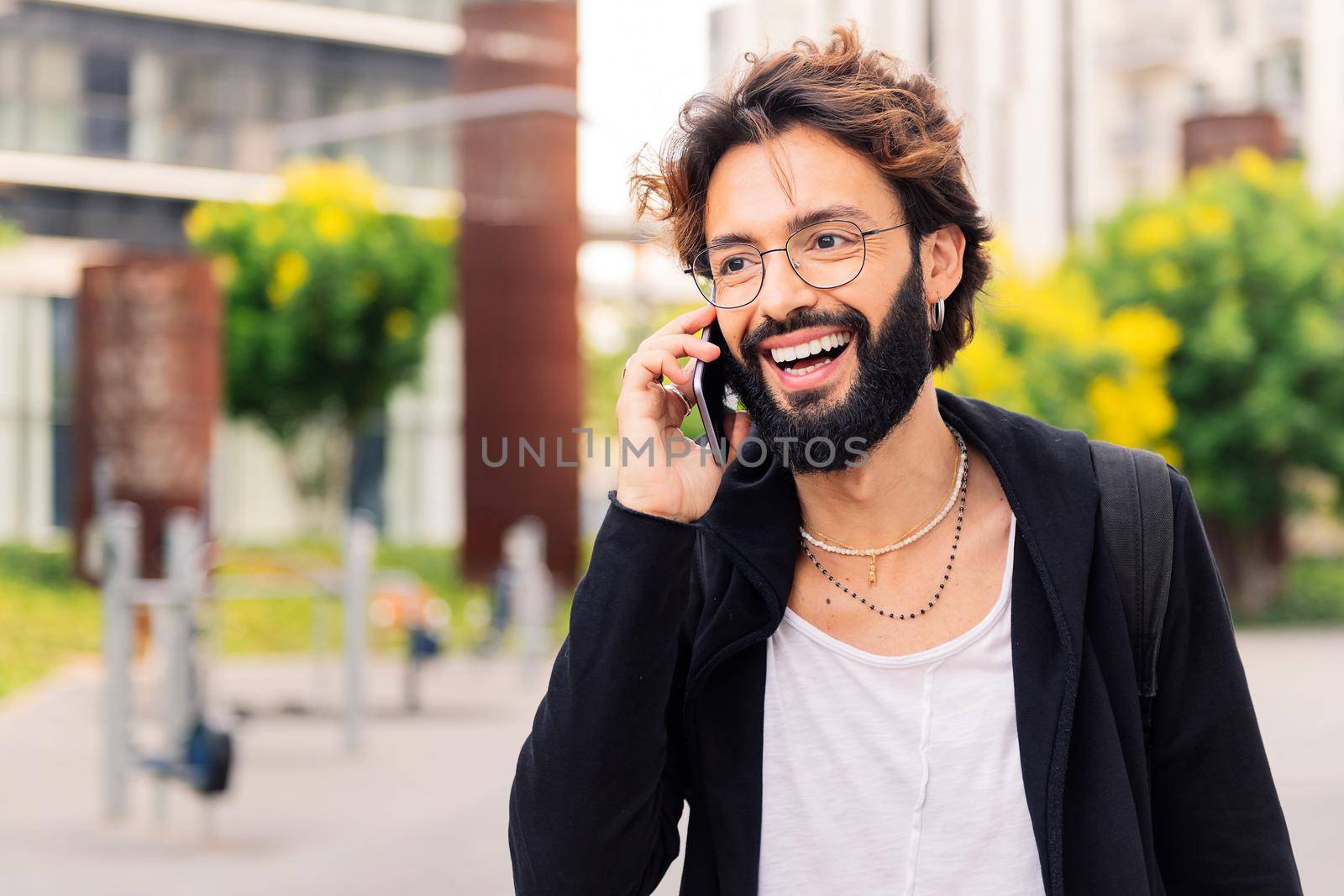stylish young man with smiling happy while talking on mobile phone in the city, concept of urban lifestyle and technology of communication, copy space for text