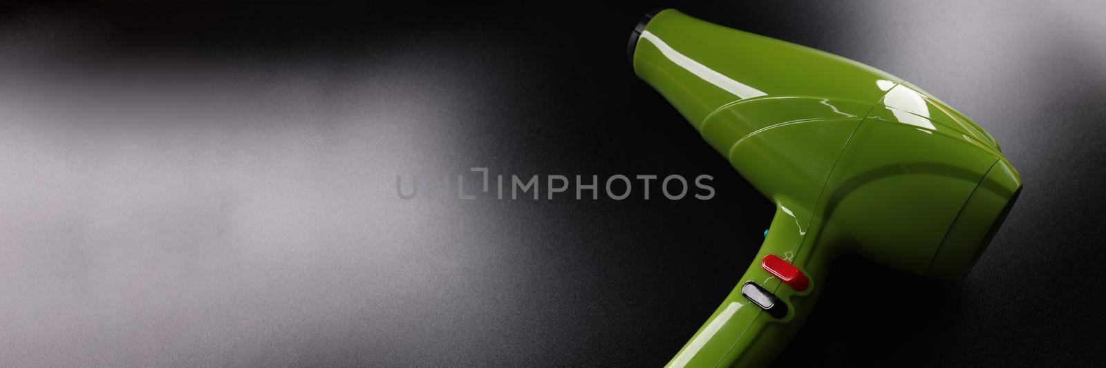 Closeup of green professional hair dryer against dark background. Hair care concept