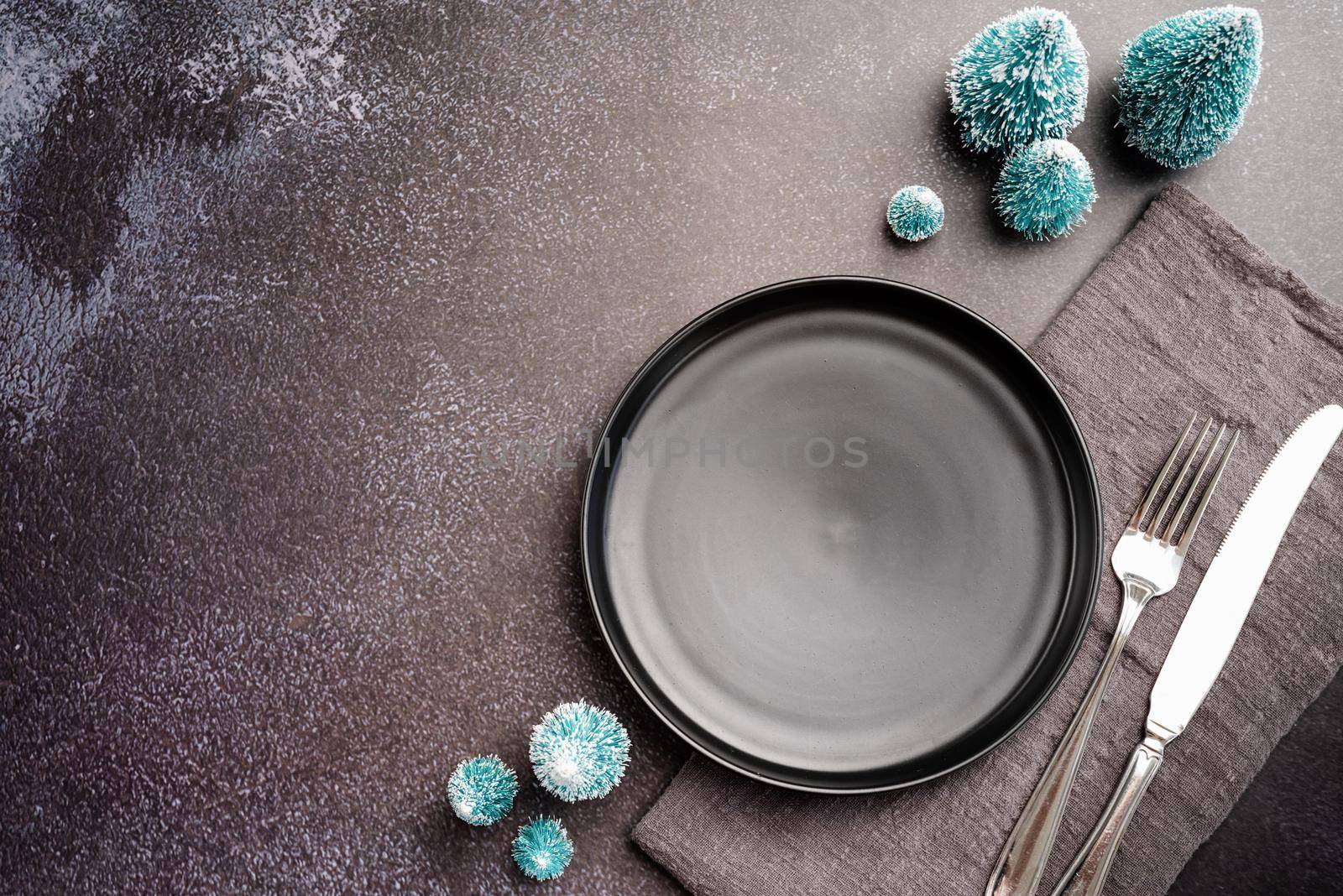 Christmas table setting with black dishware, silverware and green decorations on dark background. Top view flat lay