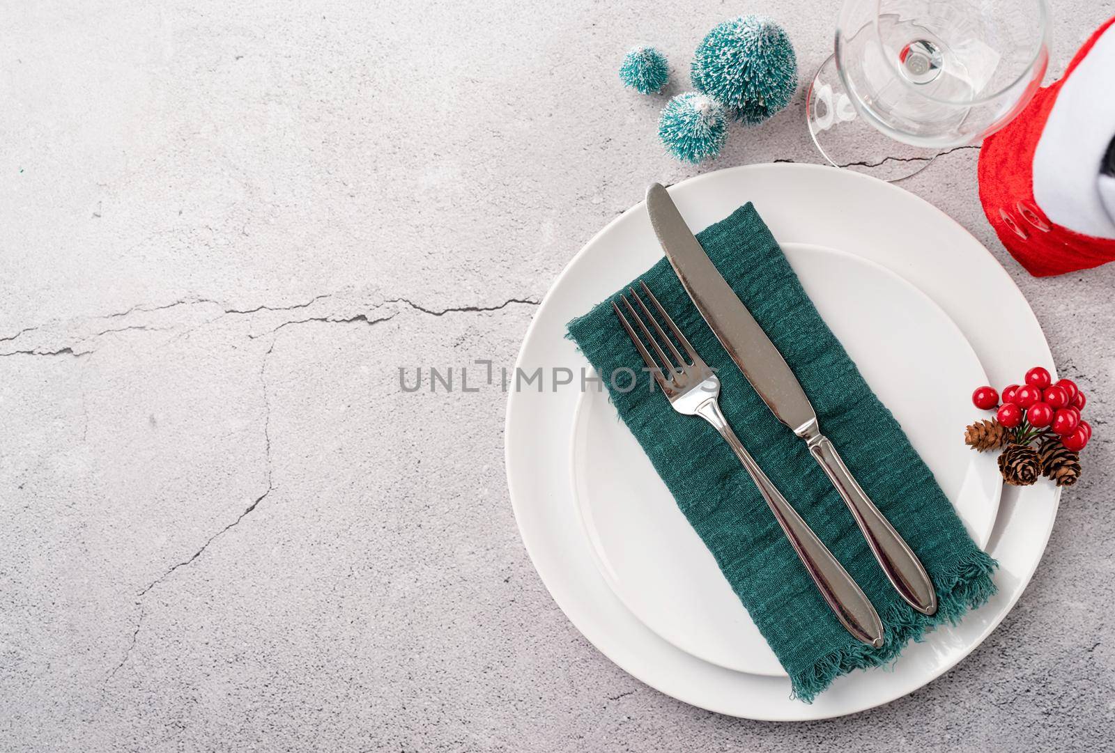 Christmas table setting with white dishware, silverware and red and green decorations on white wooden background. Top view, flat lay