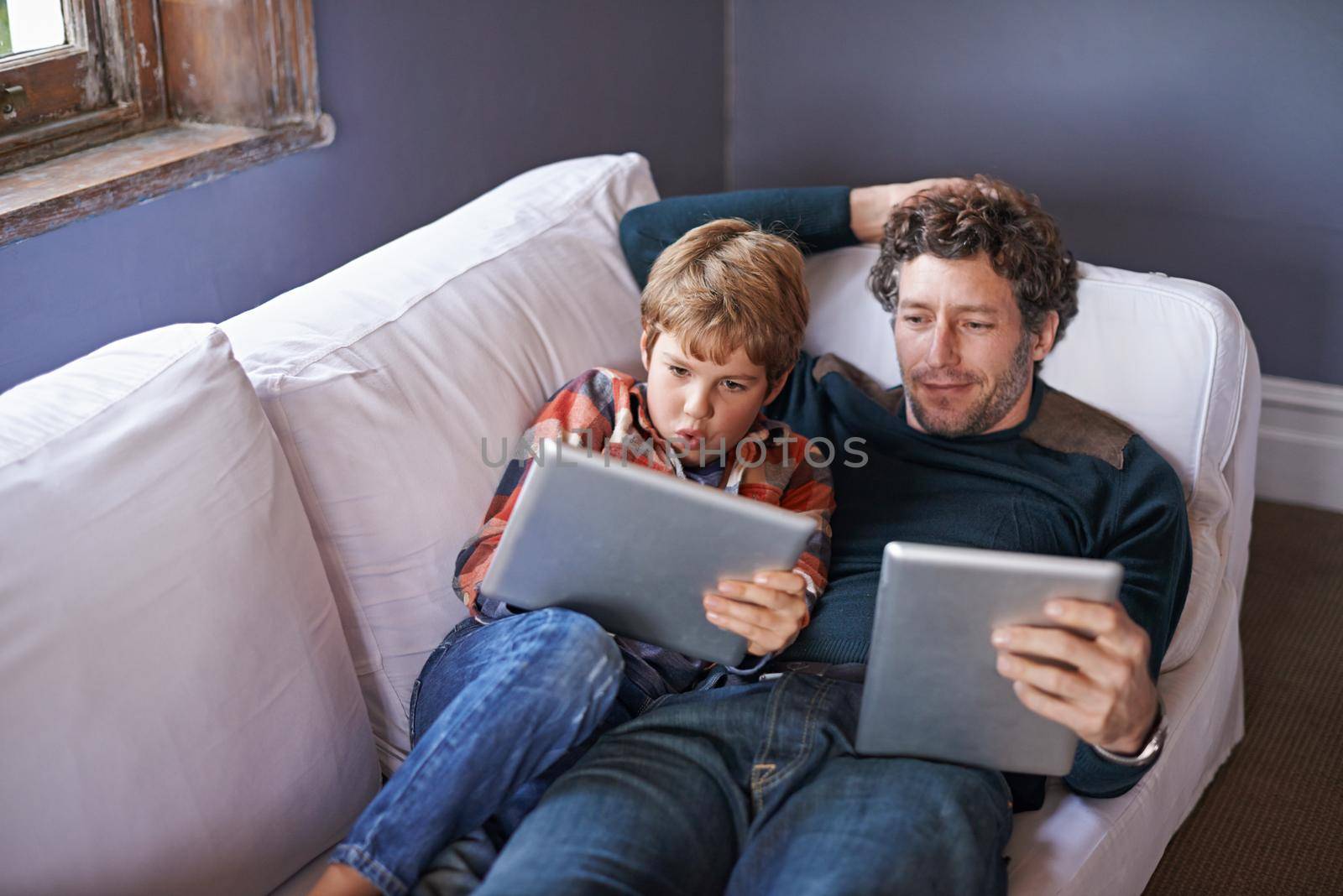 Leisure in the lounge. a father son lying on the couch together while using digital tablets. by YuriArcurs