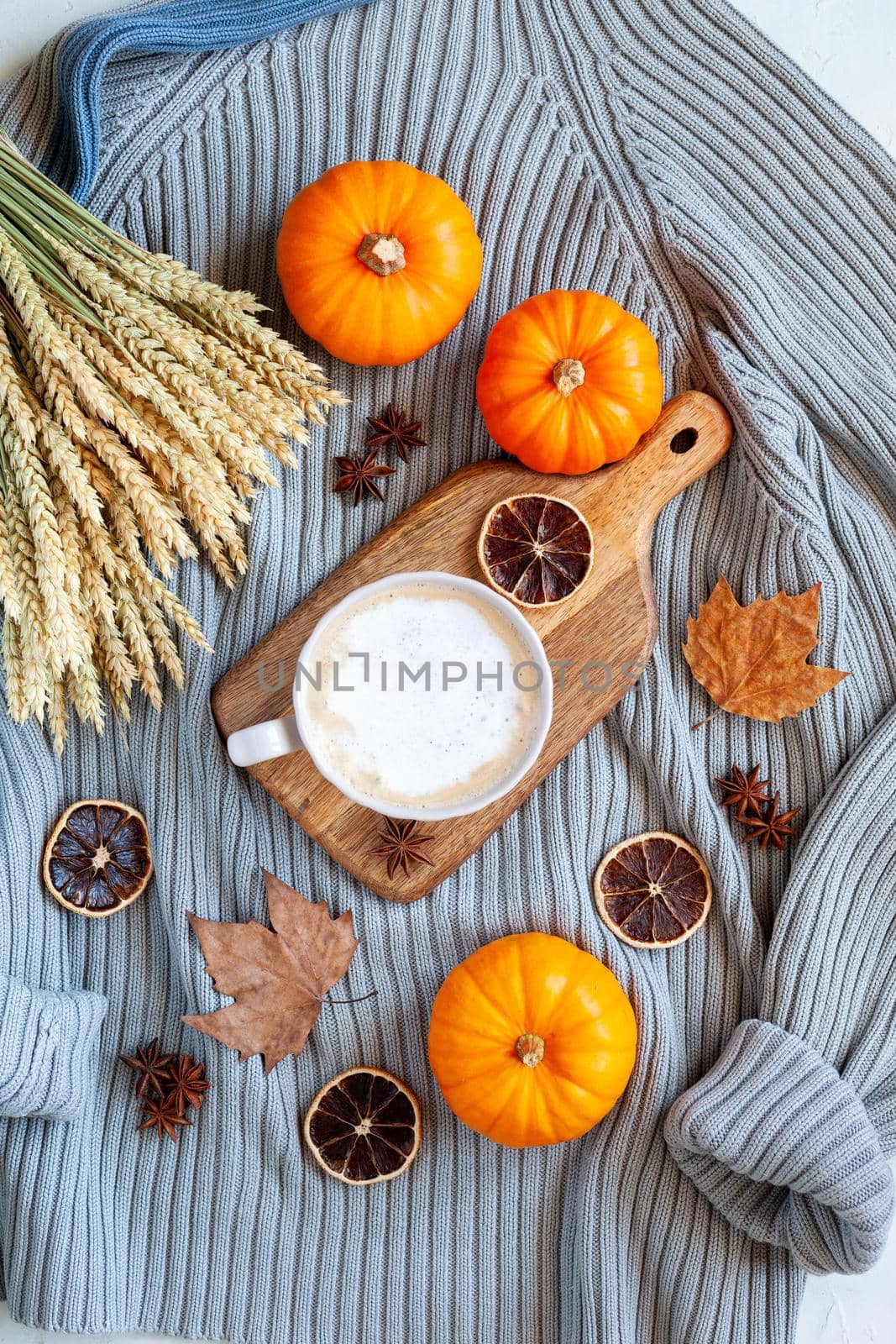 autumn flatlay composition with warm sweater, hot drink, mini pumpkins, dry leaves and dry orange slices