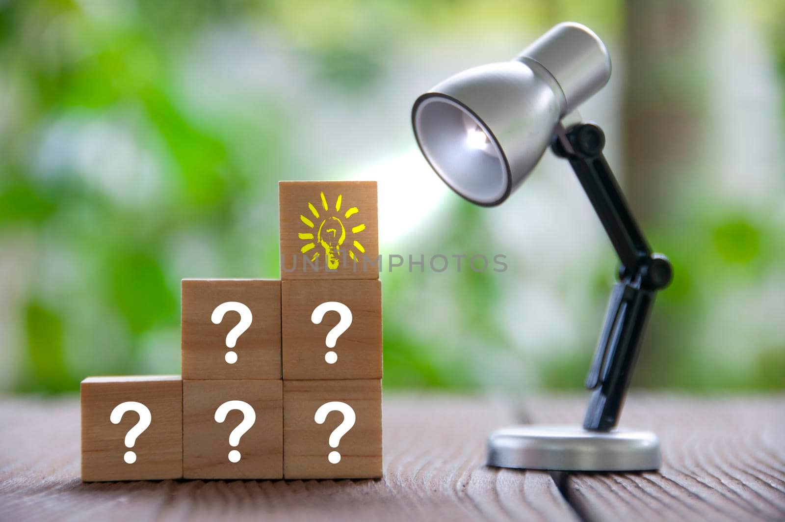 Question marks and light bulb on wooden blocks with table lamp shining. Ideas concepts.