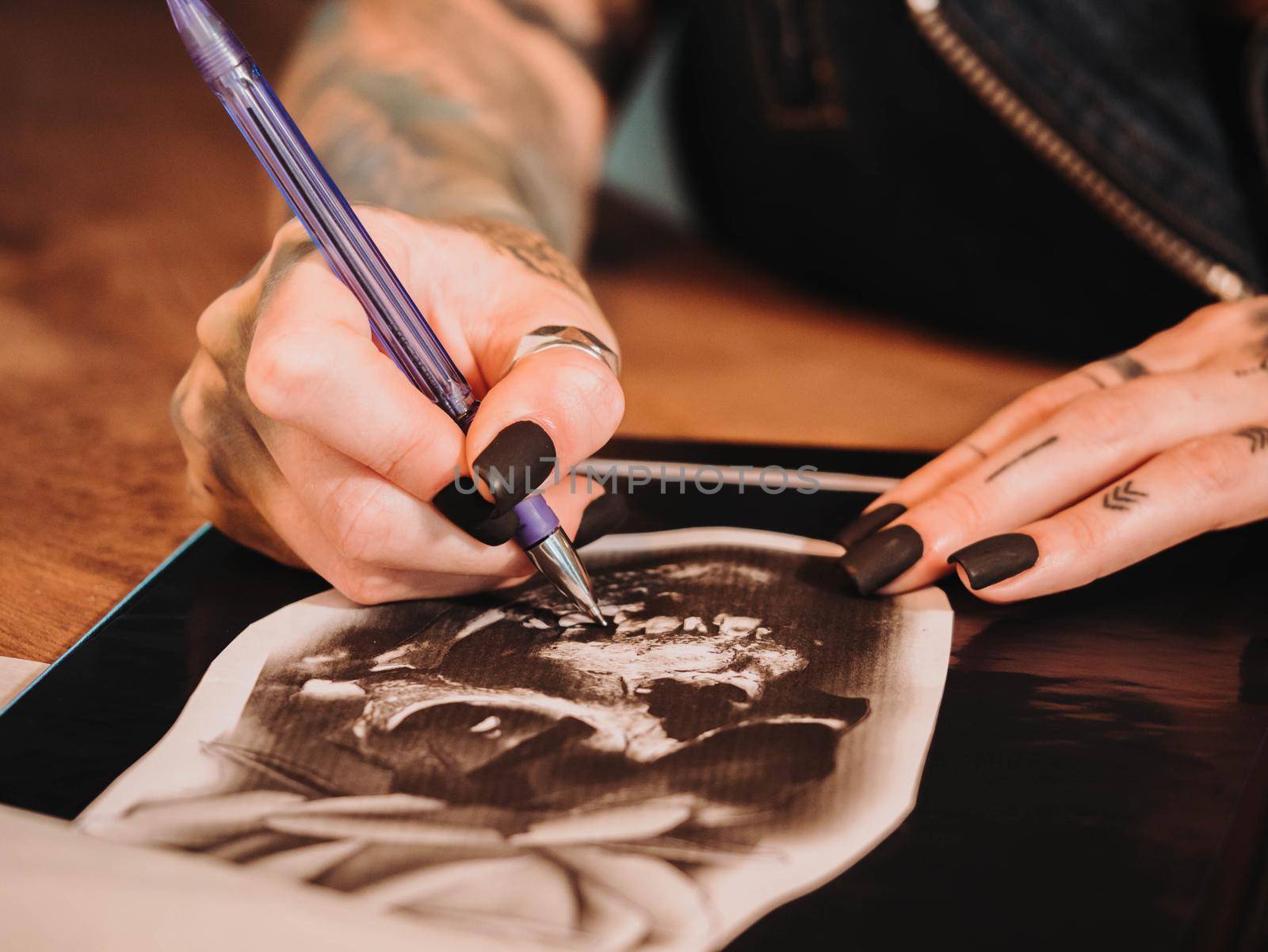 Tattoo artist drawing illustration of skull inside ink studio. Woman with black nails and rings at work. New fashion lifestyle artistic trends concept . Warm cinematic filter.