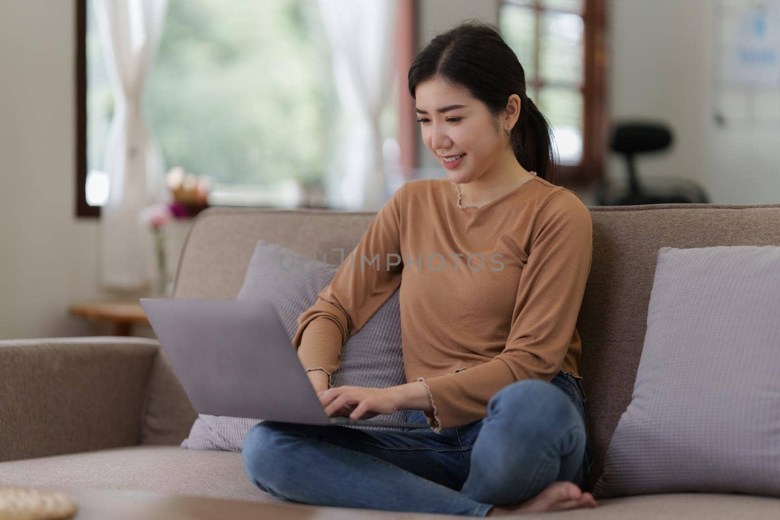 Asian woman checking social media by laptop sitting on sofa at home. lifestyle concept by itchaznong