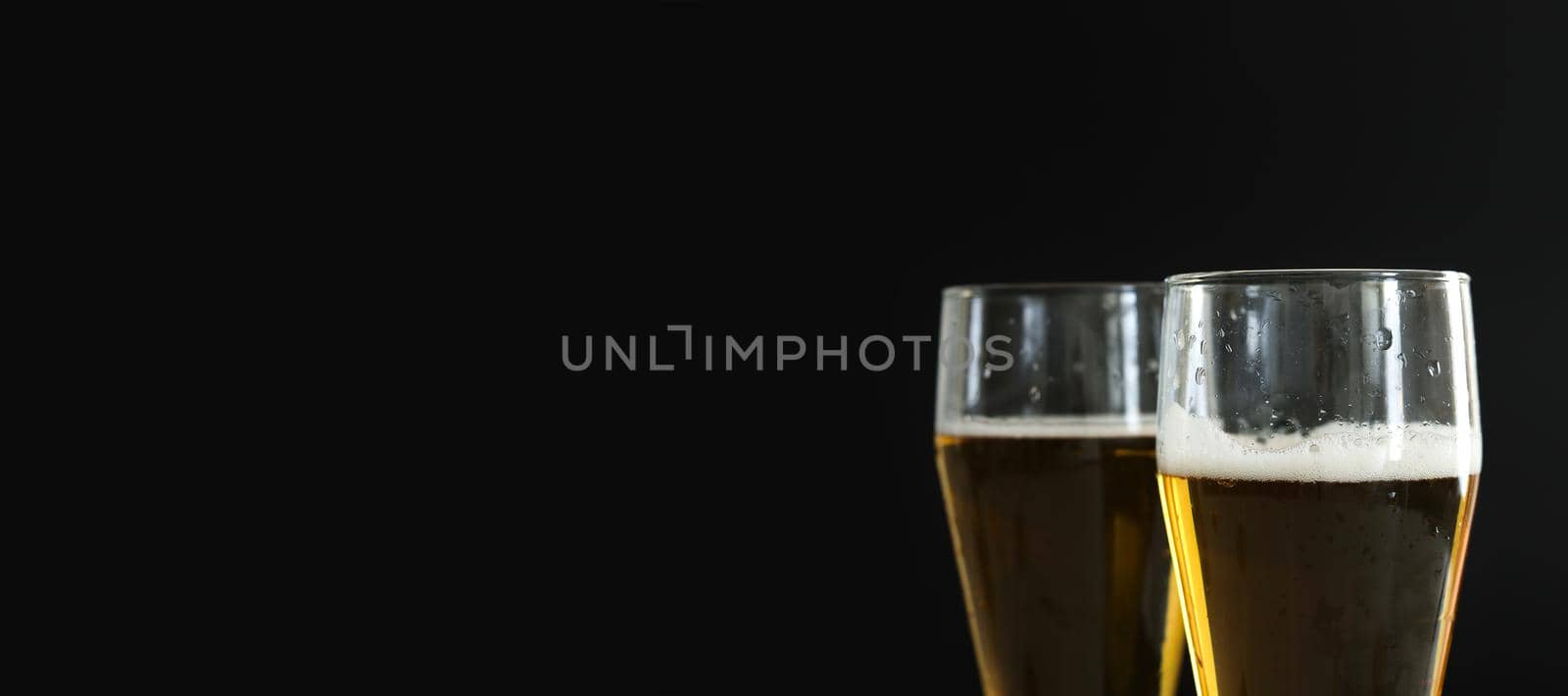 Two frosty glasses of cold golden beer with bubbles on the black background. Free space for text, copy space, banner. Drinking alcohol on party, holidays, Oktoberfest or St. Patrick's Day