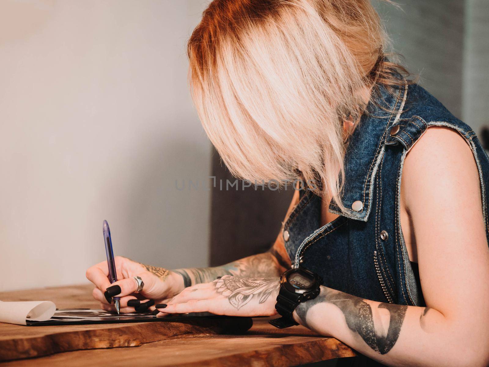 Tattoo artist drawing illustration of skull inside ink studio. Woman with black nails and rings at work. New fashion lifestyle artistic trends concept . Warm cinematic filter.