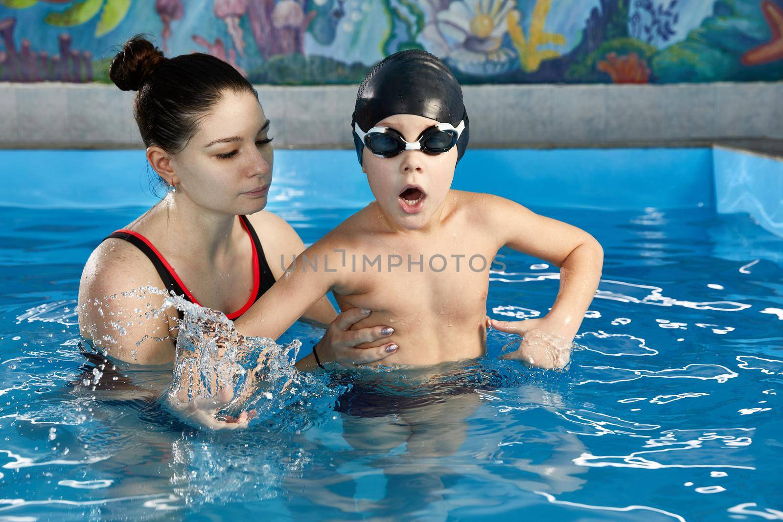 Boy learning to swim in pool with a teacher