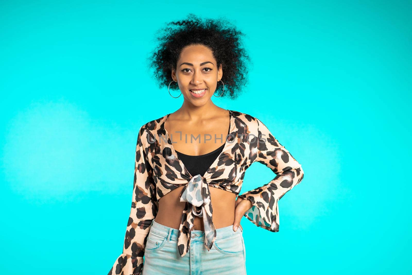 Pretty african woman with afro hair in leopard top smiling to camera over blue wall background. Cute mixed race girl's portrait. High quality photo