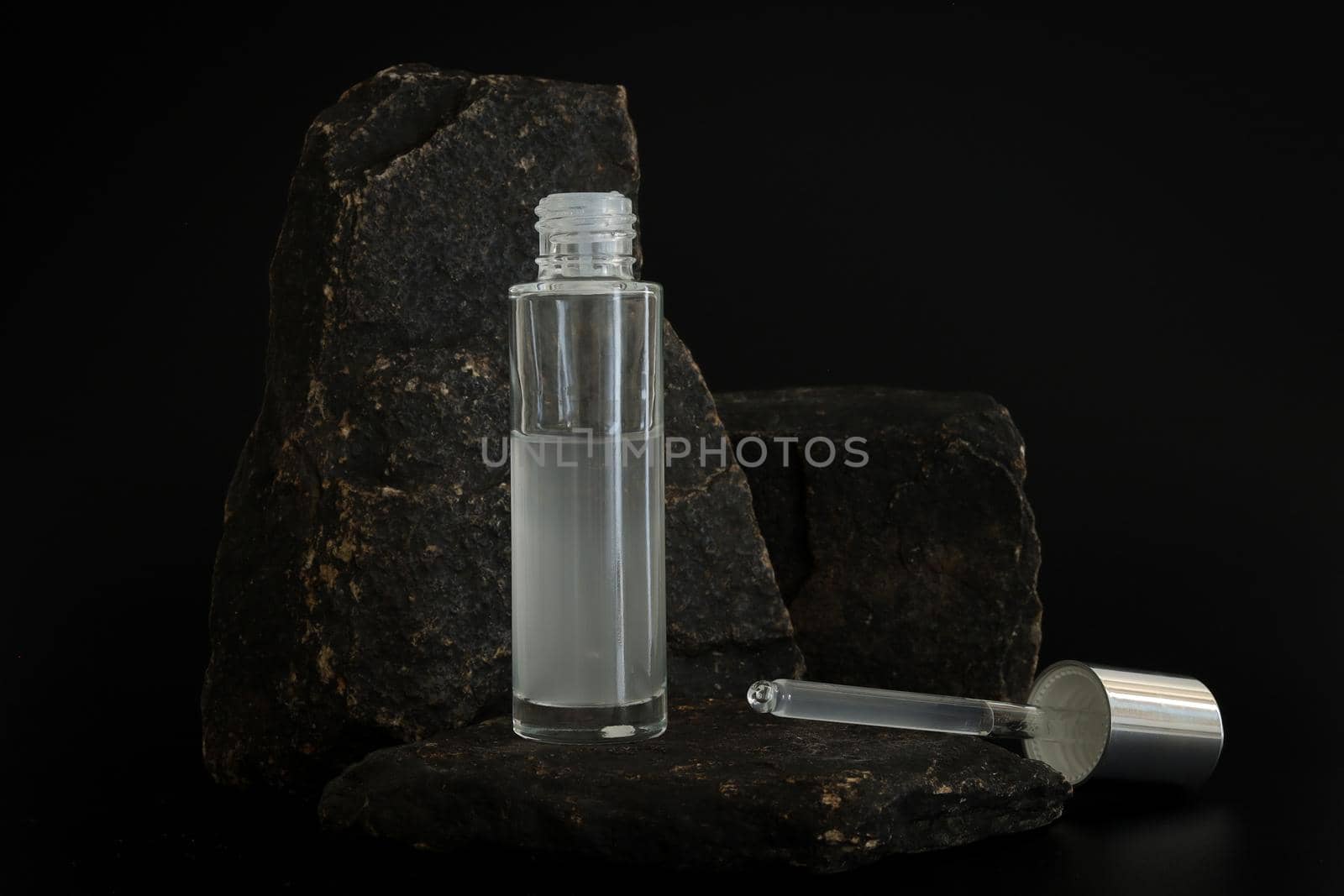 Unbranded natural cosmetic serum packaging standing on stone podium. Serum presentation on the black background. Mockup. Trending concept in natural materials. Natural cosmetic, skincare. by creativebird