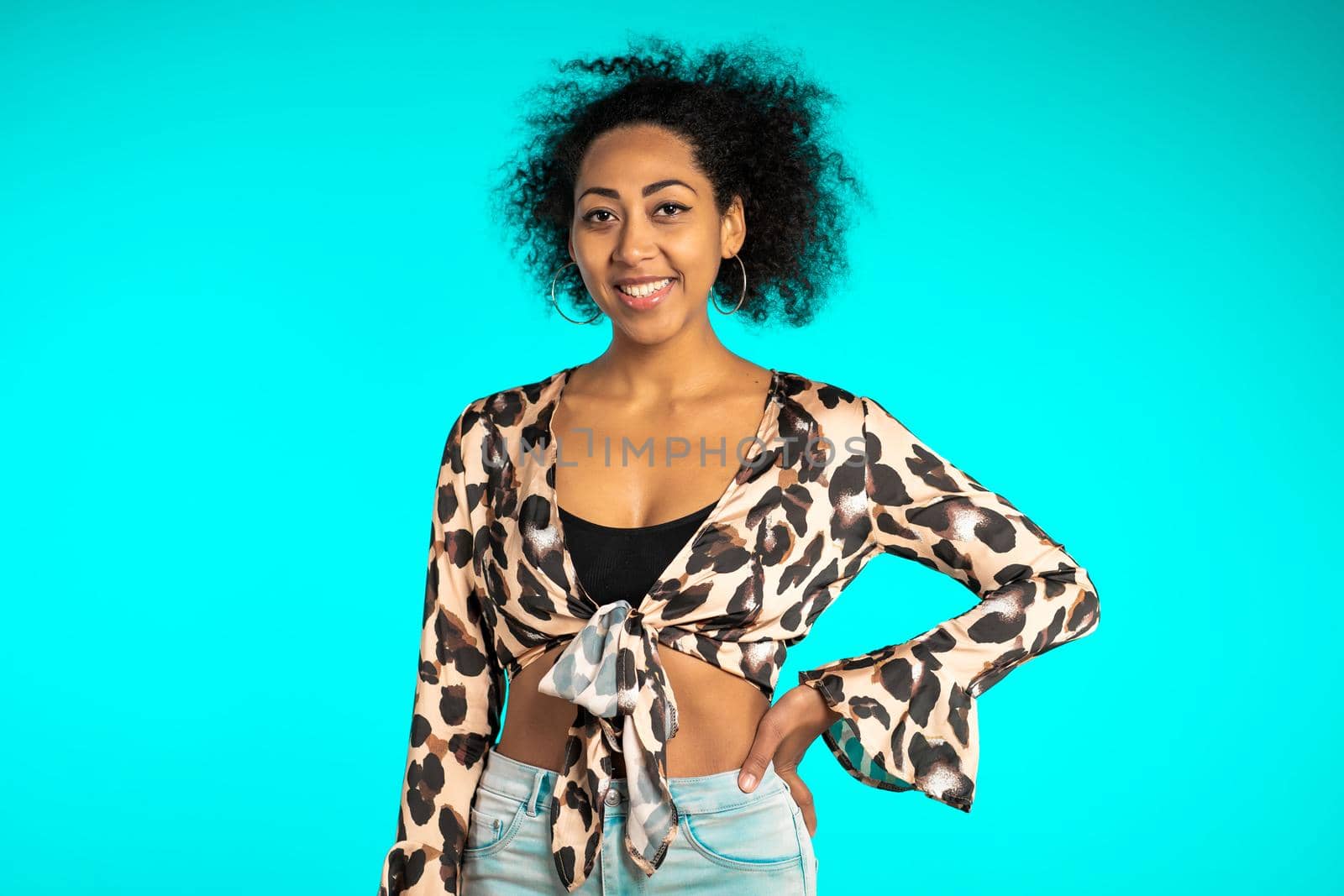 Pretty african woman with afro hair in leopard top smiling to camera over blue wall background. Cute mixed race girl's portrait. High quality photo