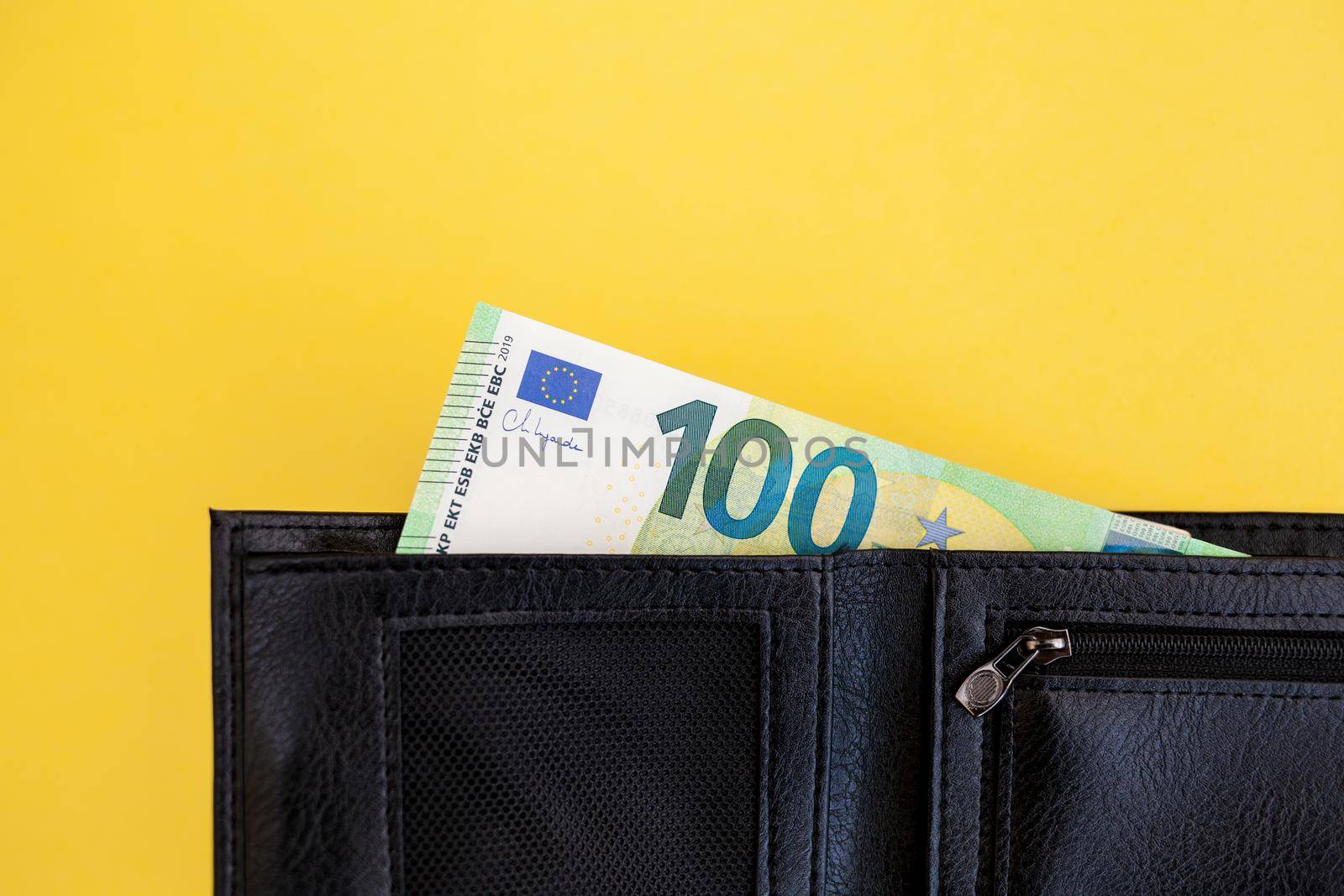 A hundred euro banknote sticks out of a black wallet on a yellow background. cash paper currency, payment, earning and savings, european currency, money and finance concep. space for text