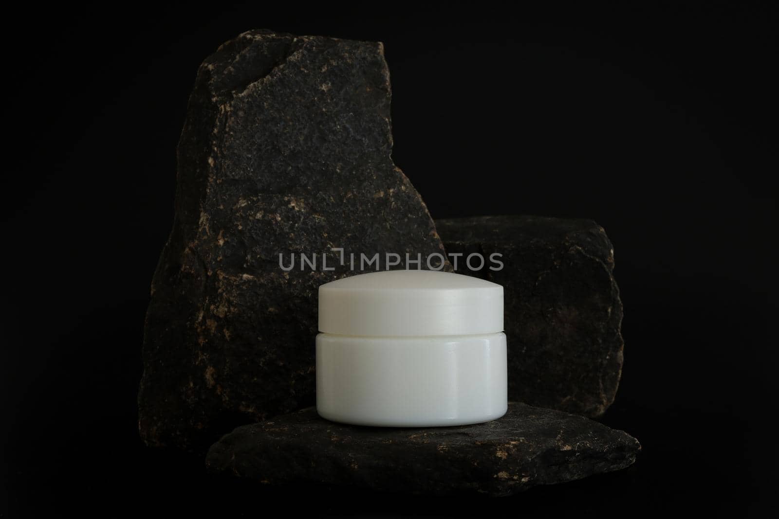 Unbranded natural cosmetic cream packaging standing on stone podium. Cream presentation on the black background. Mockup. Trending concept in natural materials. Natural cosmetic, skincare. by creativebird