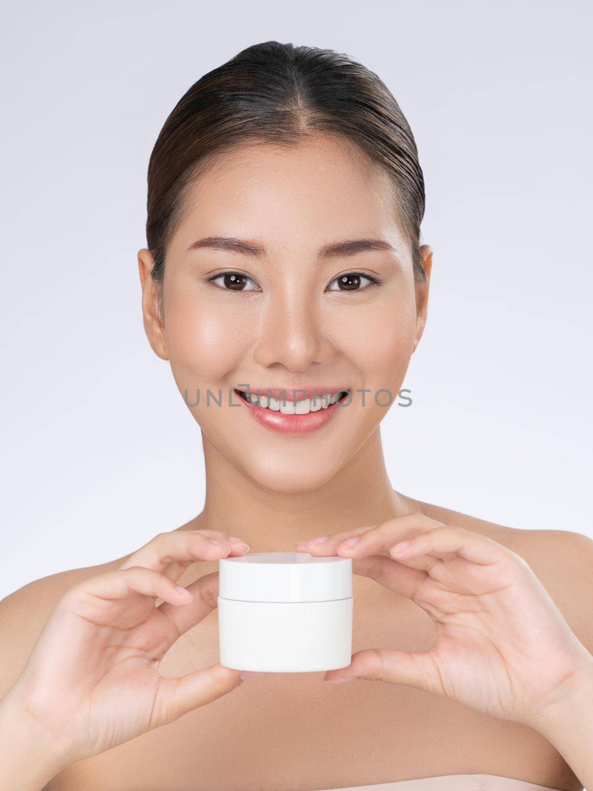 Gorgeous woman smiling holding mockup product for advertising text place, light grey background. Concept of healthcare for skin, beauty care product for advertising.