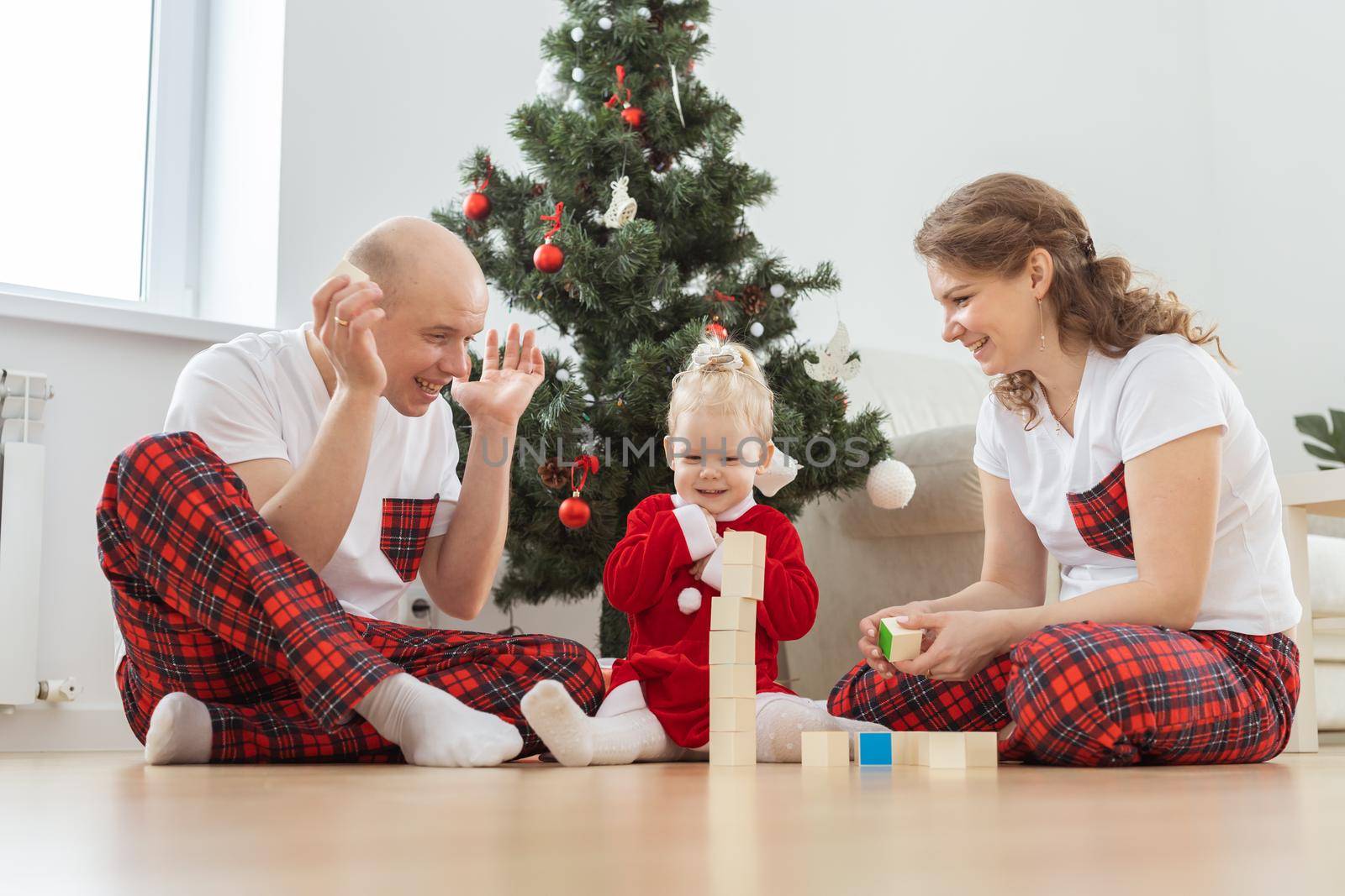 Toddler child with cochlear implant plays with parents under christmas tree in new year and winter holidays - innovating medical technologies for hearing aid and diversity by Satura86