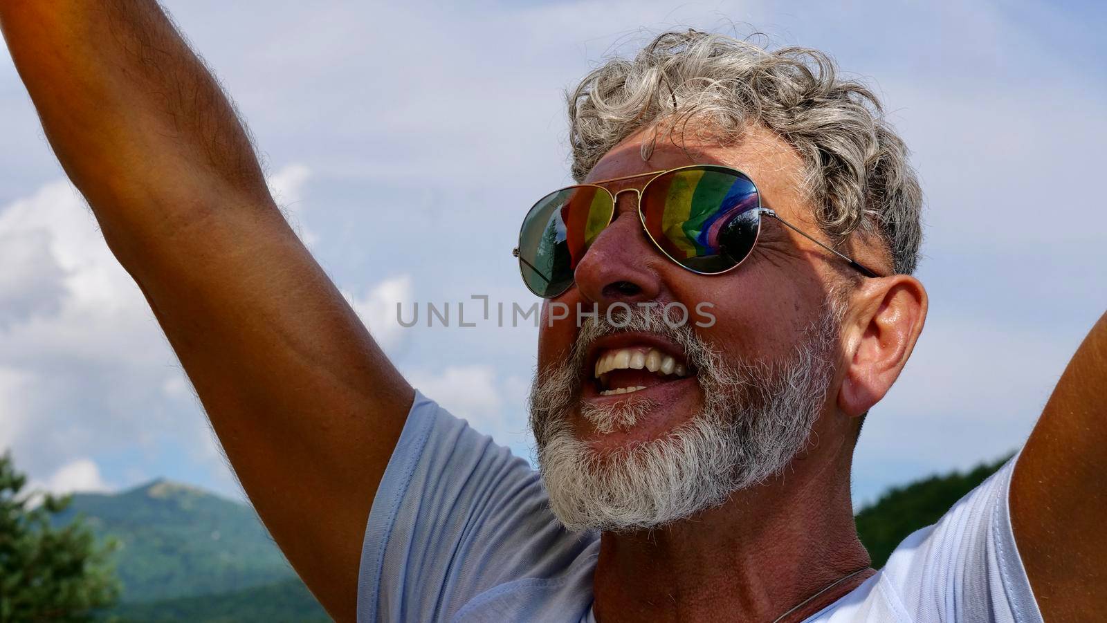 Gay gray-haired holds LGBT flag against a sky by OksanaFedorchuk