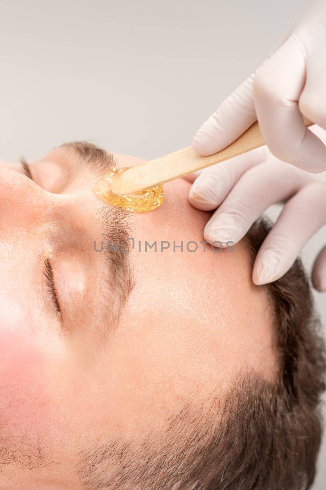 Beautician applying wax paste between eyebrows during the procedure of waxing in the beauty salon