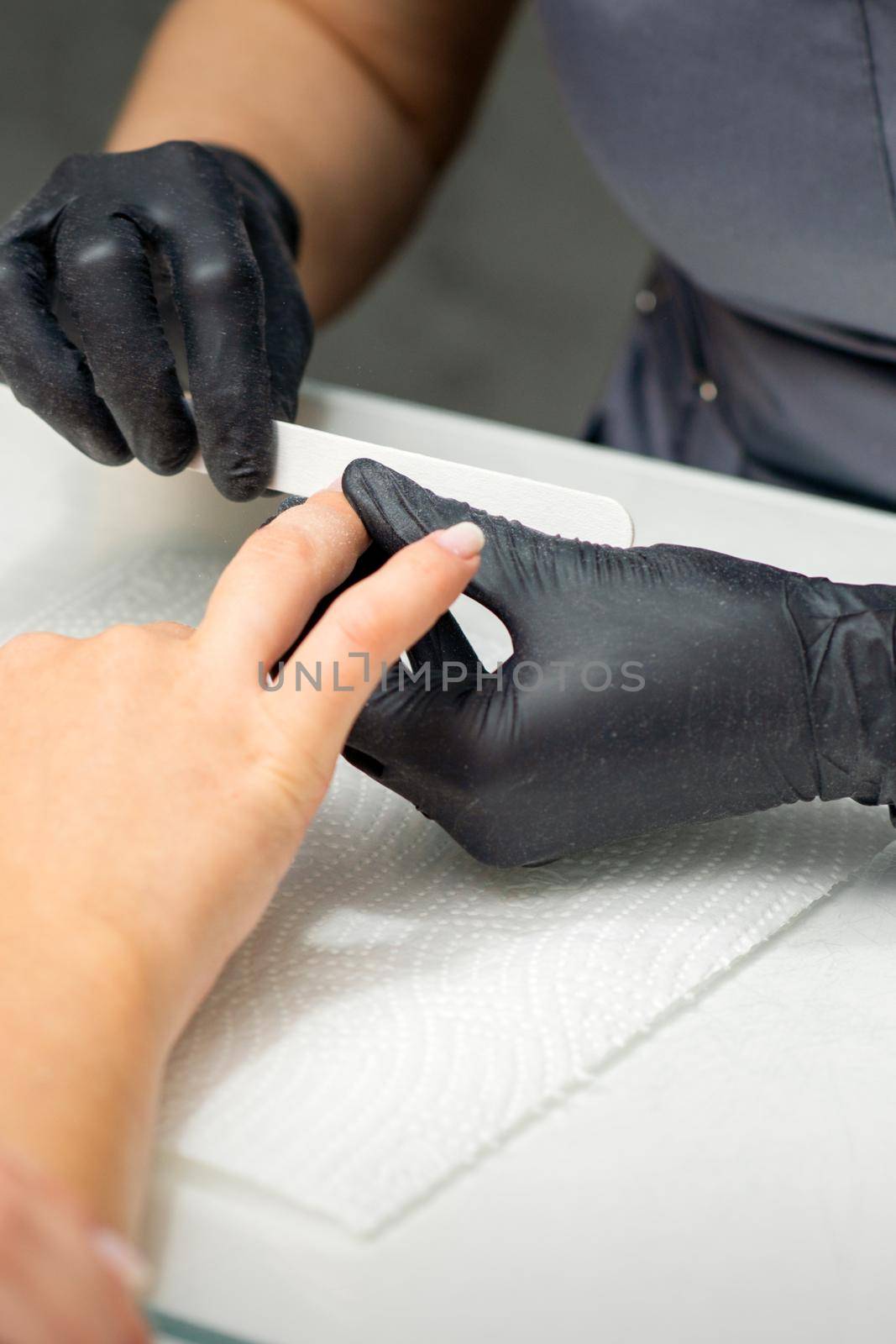 Woman receiving a manicure with nail file by a manicure master in a nail salon