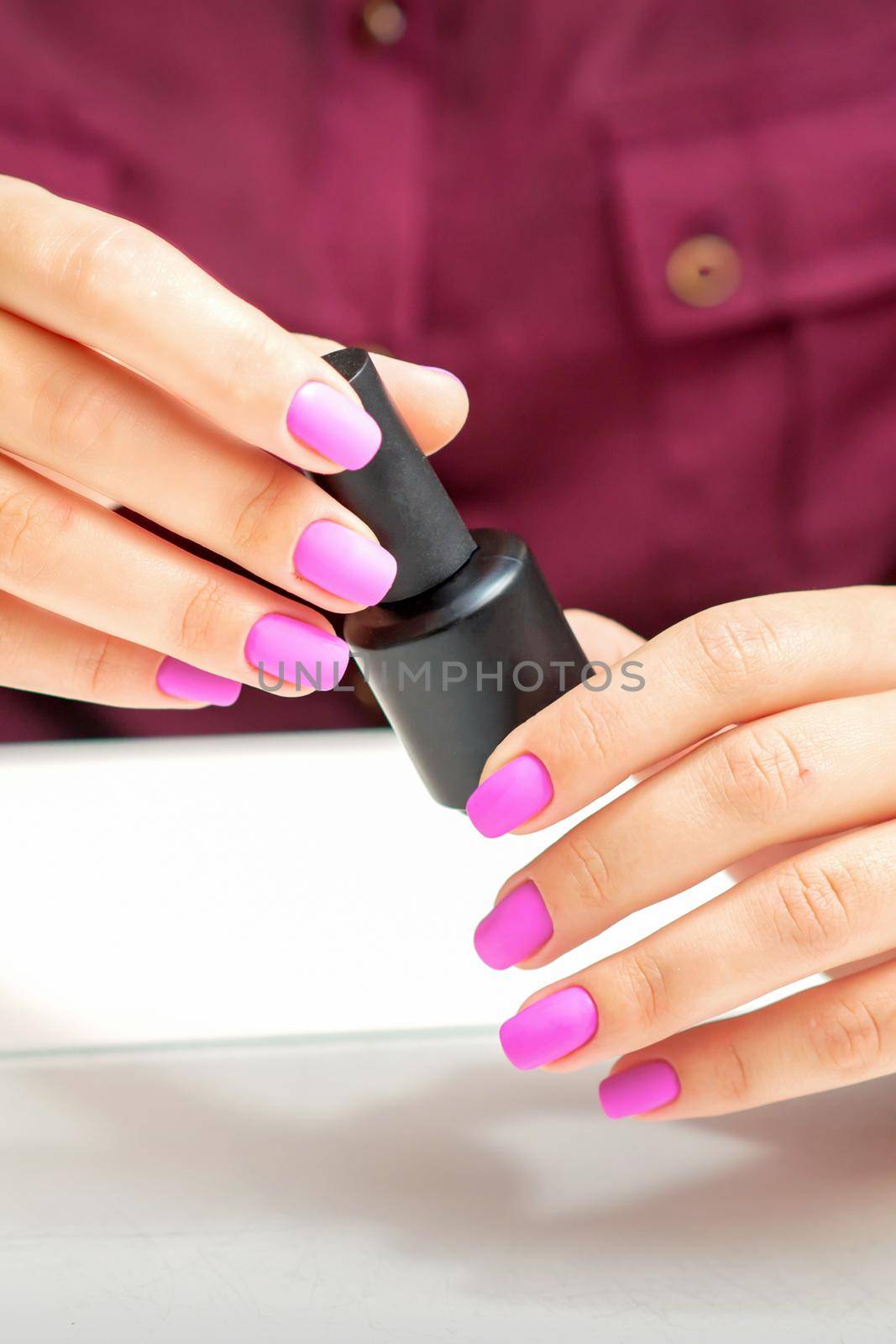 White woman holding nail polish black bottle with painted pink nails close up