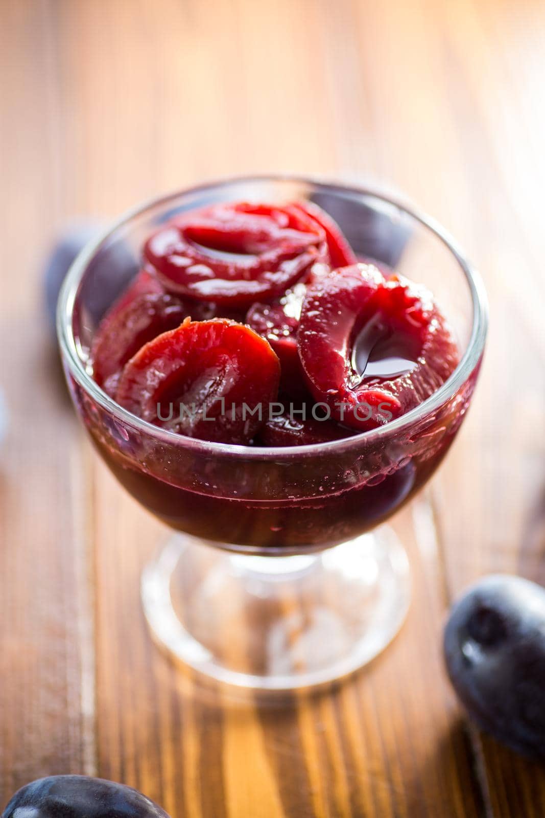 Sweet plums in syrup, in a glass bowl on a wooden table.