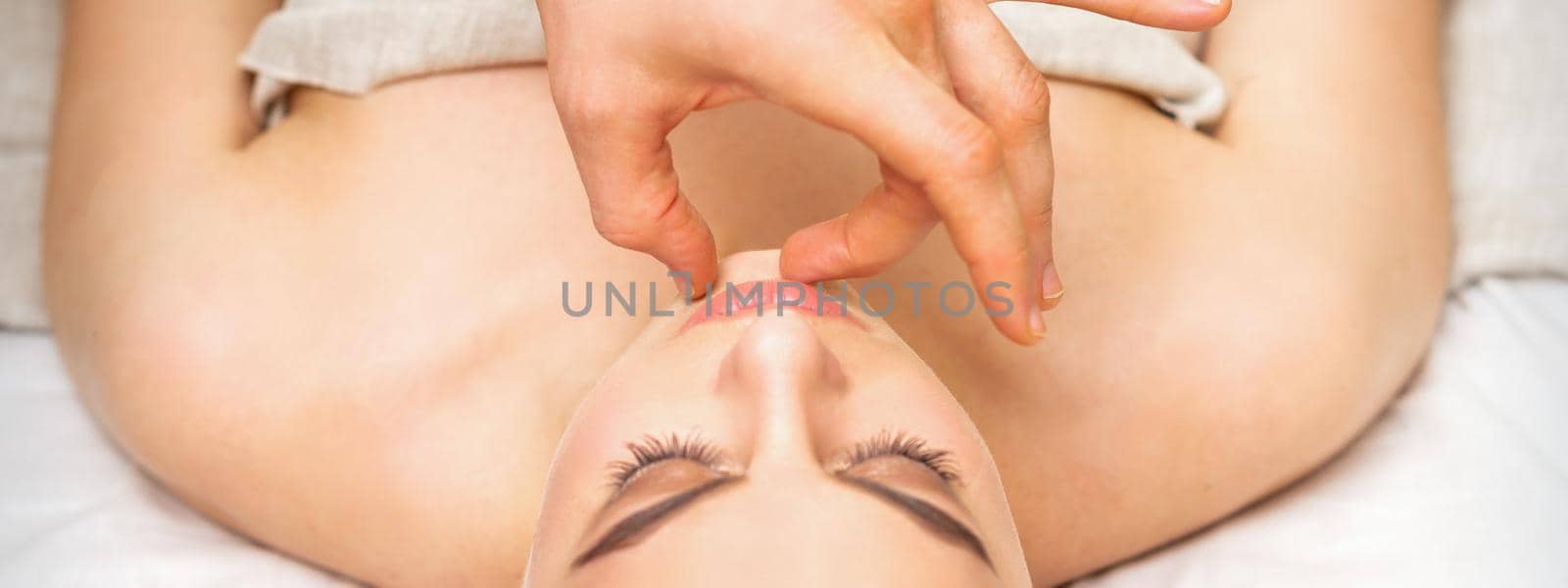 Young caucasian woman receiving chin massage by male therapist fingers in spa salon