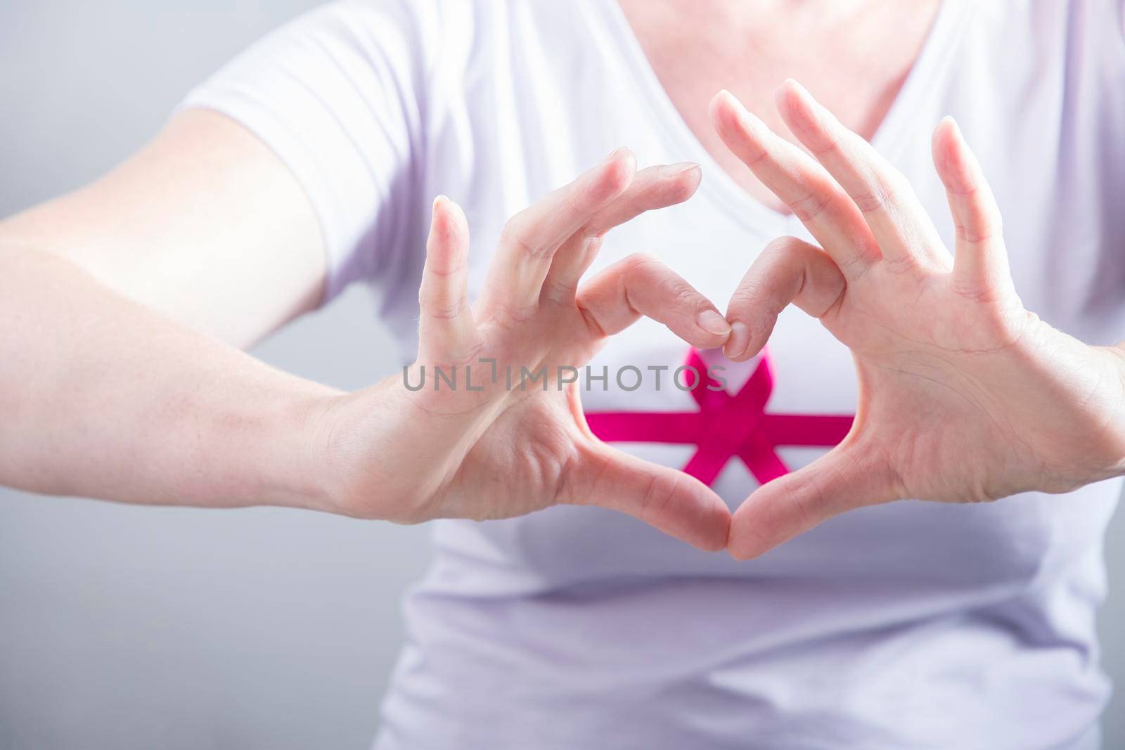 woman making heart sign with fingers on breast cancer protection symbol background. High quality photo
