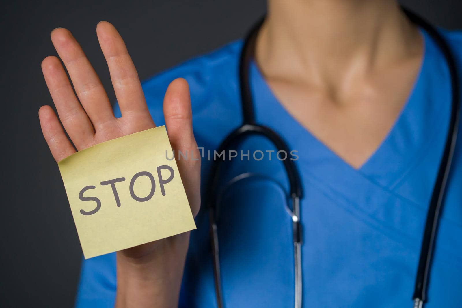 A woman doctor holds a paper in her palm, a note with the inscription "stop" in her hand. A young nurse in a medical suit and with a stethoscope transmits a message