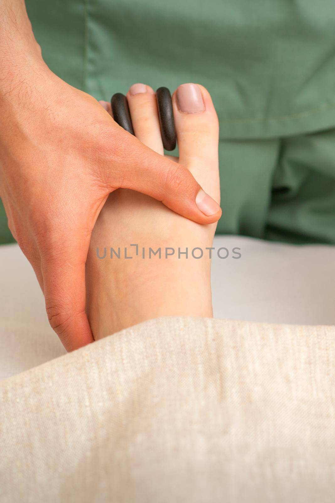 Massager doing feet and toes massage with rocks between a female toes